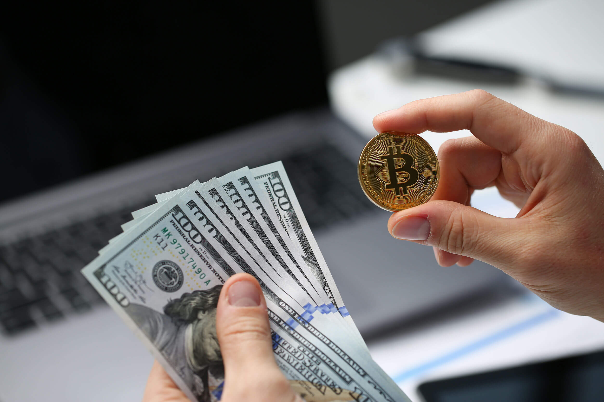 Photo of a person holding US dollars and a gold coin marked as a Bitcoin, representing how experienced legal guidance on business and commercial matters including entering into B2B Bitcoin transactions.