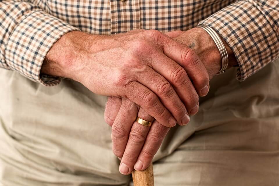 A close-up image of the hands of an older man holding a walking stick, representing the need for elder care planning in WV, KY, and OH and how an experienced attorney for long-term care planning can help.