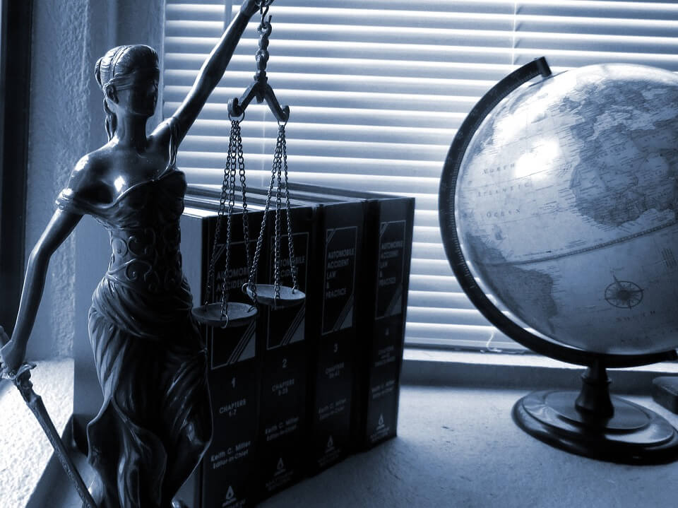 Image of Lady Justice on a shelf next to a globe and code books, representing the legal knowledge and skill that WV municipal defense lawyers need to guide political subdivisions.