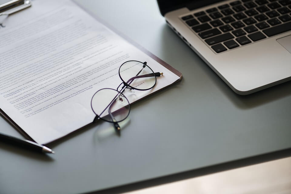 Image of a pair of glasses laying on top of a contract, representing how drafting a WV arbitration clause requires the knowledge and experience of a business lawyer.