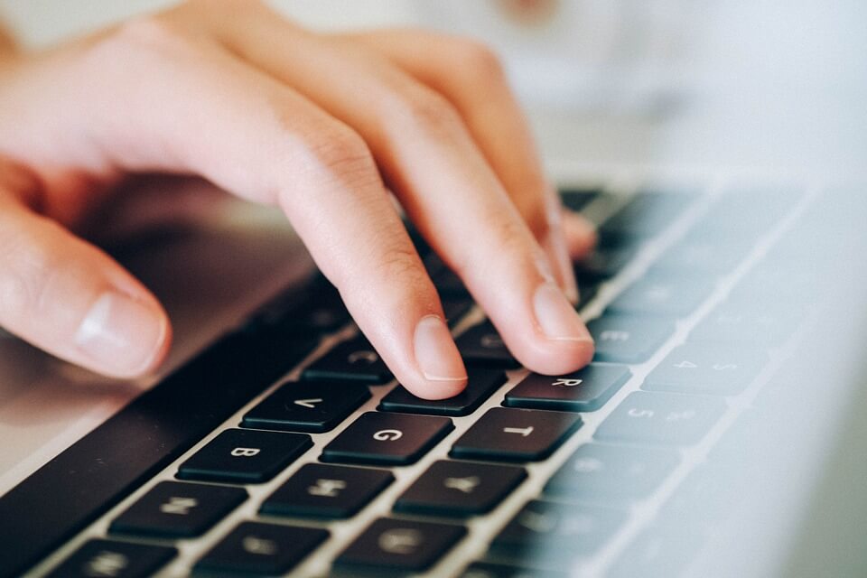 Image of a person's hand on a laptop hesitating while completing an online form, representing a person asking himself the question, 