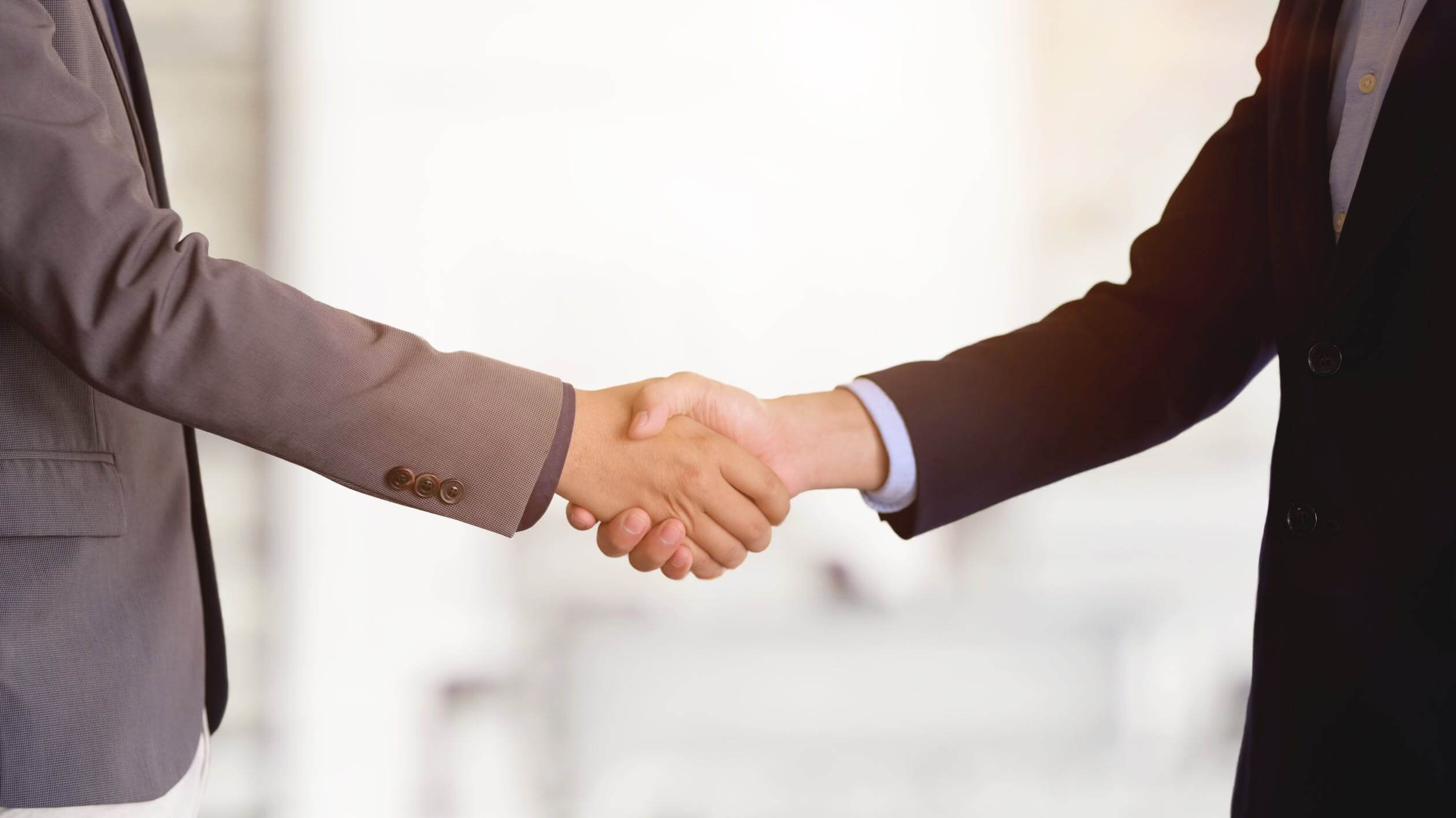 Image of two people shaking hands, representing how M&A lawyers help businesses realize the benefits of joining together and understand the the differences between types of mergers.