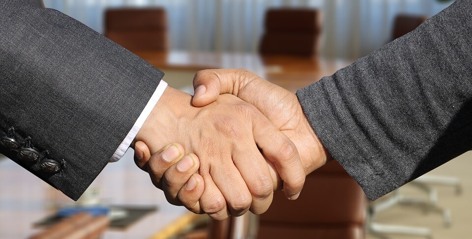 Image of people shaking hands over paperwork and a laptop, representing working with a financial planner and a West Virginia estate planning attorney to coordinate employment benefits with your estate planning strategy.