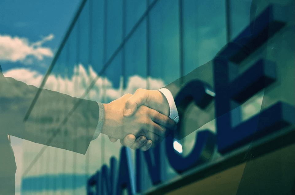 Image of two businesspeople shaking hands in front of an office building in a merger or acquisition, representing how M&A attorneys help businesses create and execute a successful M&A plan.