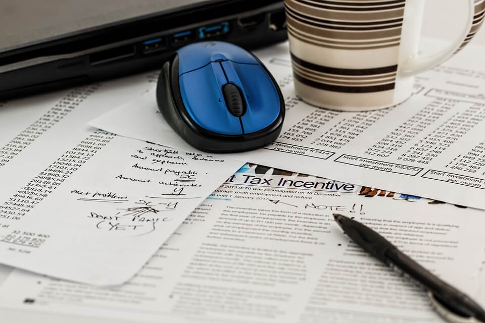 Image of paperwork with tax calculations, a computer mouse, and inkpen, representing an employee completing the new I-9 form in WV.