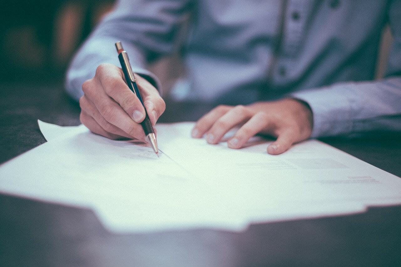 An image of hands signing a document that is out of focus, representing the need for clarifying the intent of the deceased in WV undue influence will and trust cases with the help of an attorney.